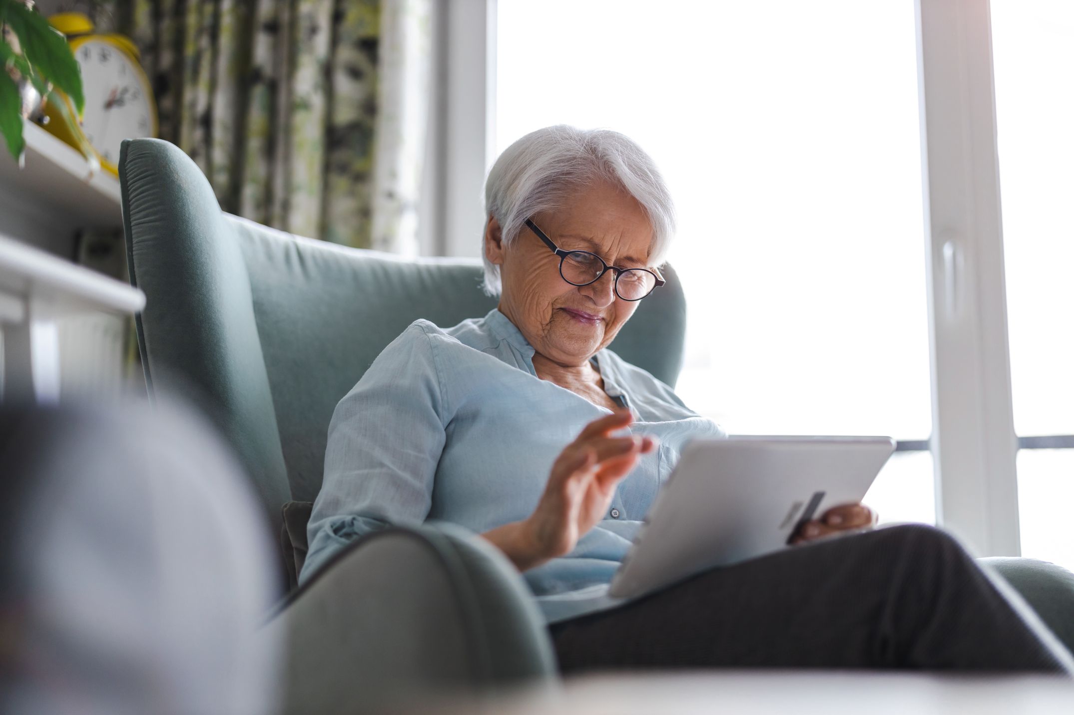 Senior woman sits at home using digital tablet.